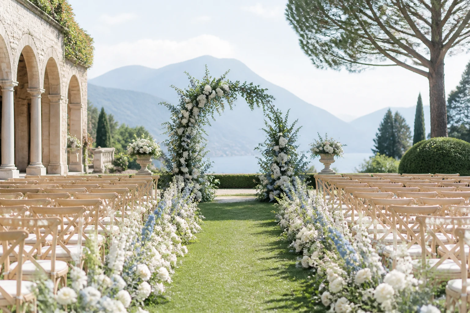 Pale stone wedding terrace prepared with white chairs, blue flowers, and a view across the water