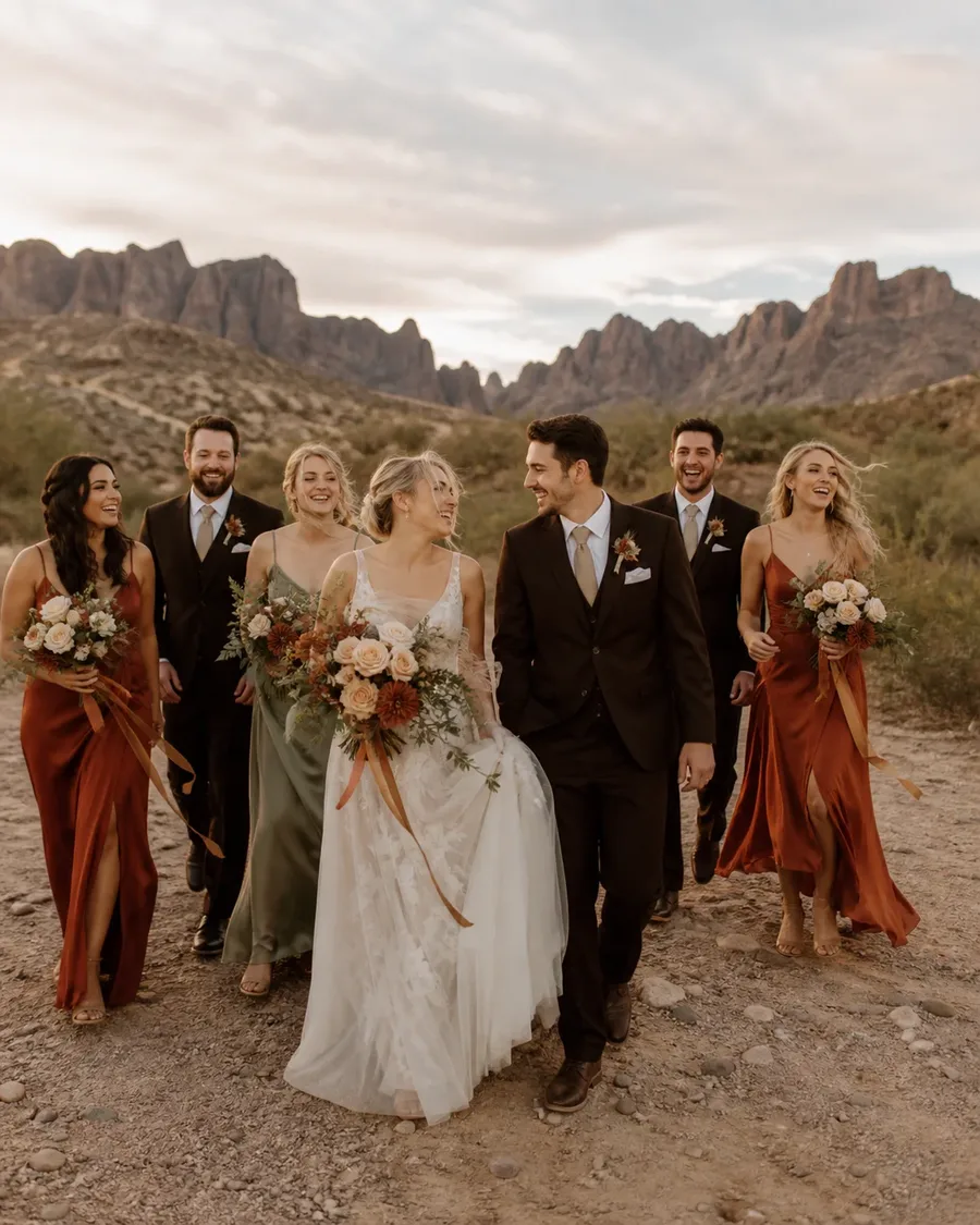 Wedding party in rust, sage, cream, and dark formalwear walking through a desert wash