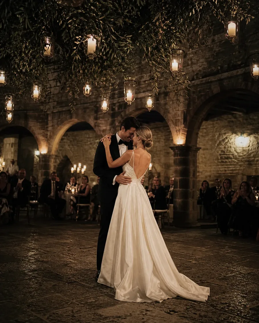 Newlyweds sharing their first dance beneath candle lanterns in a stone courtyard