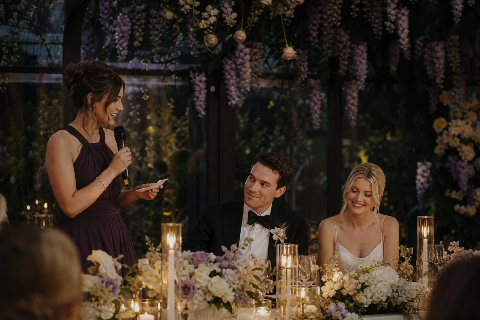 Bridesmaid giving a toast beside newlyweds at a candlelit conservatory reception